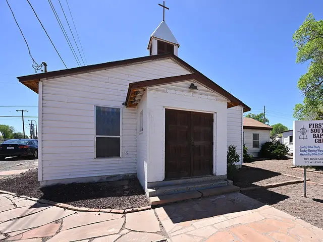Small white wooden First Southern Baptist Church with a cross-topped steeple and a signboard listing service times in Ash Fork, Arizona.