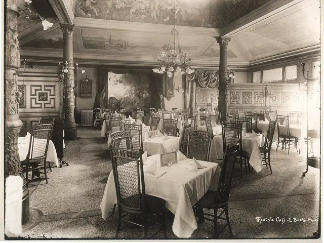 An empty historic restaurant dining room with four-seat tables, a painted ceiling and a tile floor.