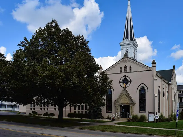 Exterior of Saint Mary Catholic Church in Hillsboro, Ohio, a cream-coloured church with a tall white steeple, seen beside a large tree.