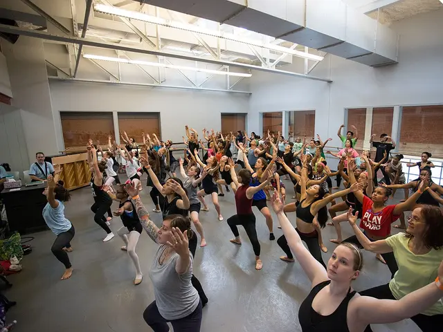 A large group of adult dancers practicing a modern dance class together in a studio.