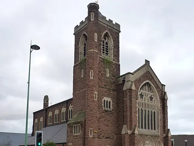 The Assemblies of the First Born Church of God, a red sandstone church with a square battlemented tower and a large pointed-arch window.