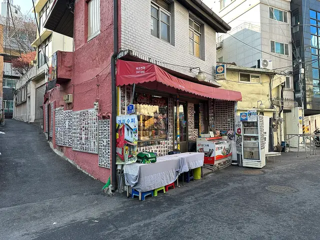A small corner grocery shop in Seoul, South Korea, with a red awning and shelves of goods visible through the window