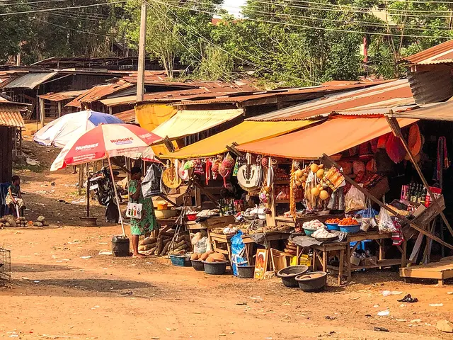 A row of market stalls with colourful awnings at Eke Awgbu Market Place, Nigeria, selling household goods and foodstuffs.