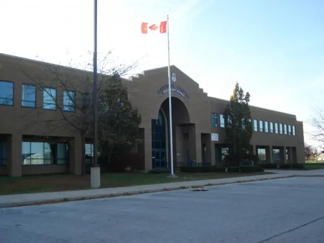 The brick exterior entrance of a Catholic high school building, with a Canadian flag flying above the doorway.